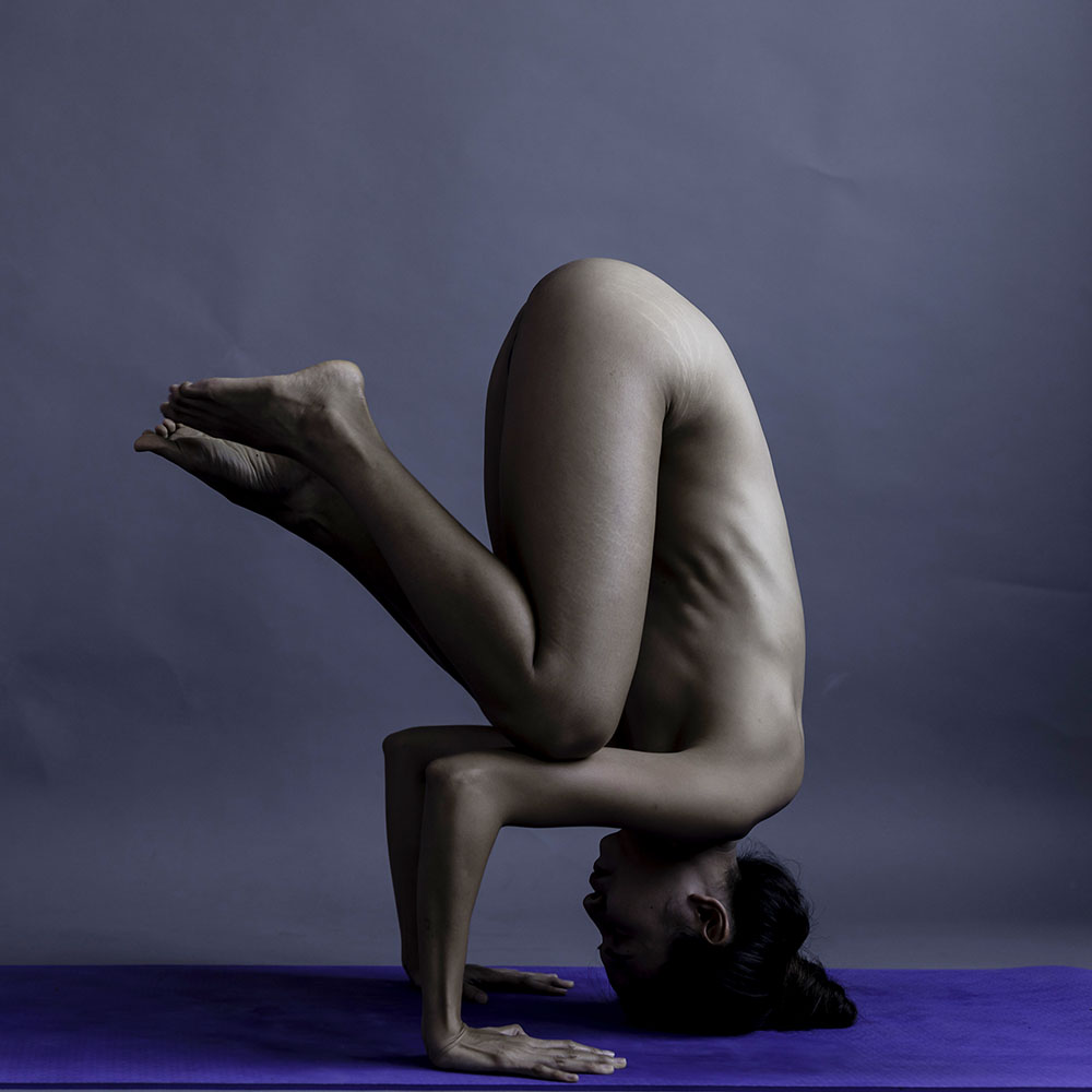 Naked fitness instructor doing yoga in the nude - head stand pose.